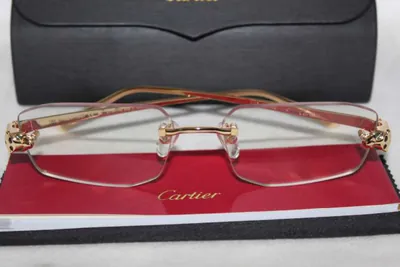 Armazón Cartier al aire dorado con la pantera en las bisagras sobre el libro rojo de la marca