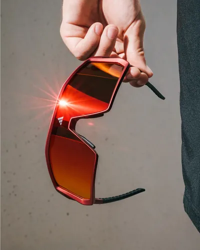 Mano sosteniendo lentes deportivos adidas de mica roja espejeada